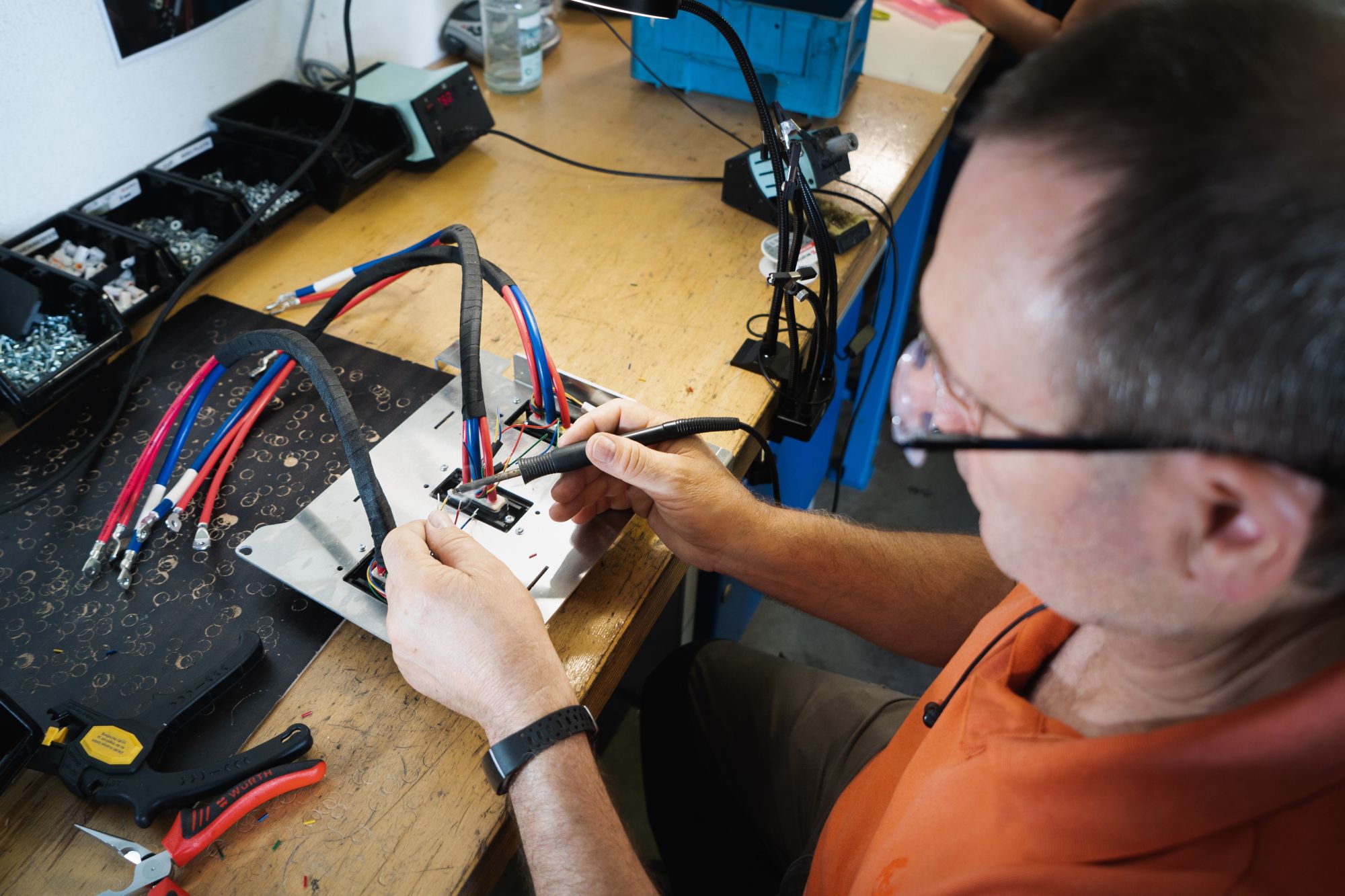 Ein Mann arbeitet als Elektroniker, ist von Kabeln umgeben und arbeitet an einer Elektronischen Schaltung auf einem Tisch